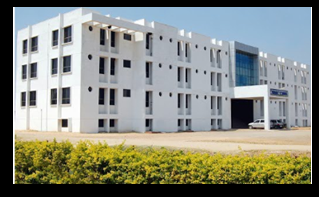 Modern white BAMS college campus building with several floors, large glass entrance and landscaped greenery in front in daylight.